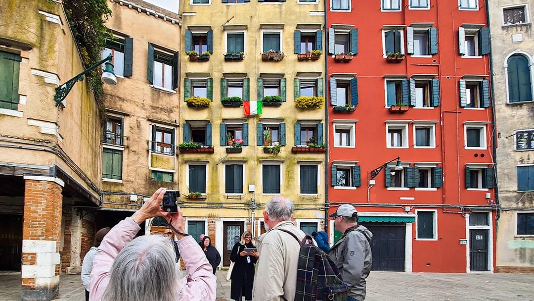 Tourists exploring a colorful Venetian square with Italian flag and historic buildings.