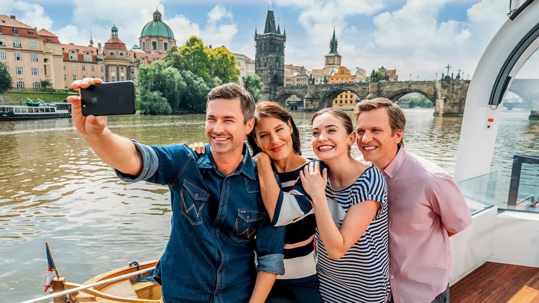 Group taking selfie on Vltava River cruise with Charles Bridge in Prague.