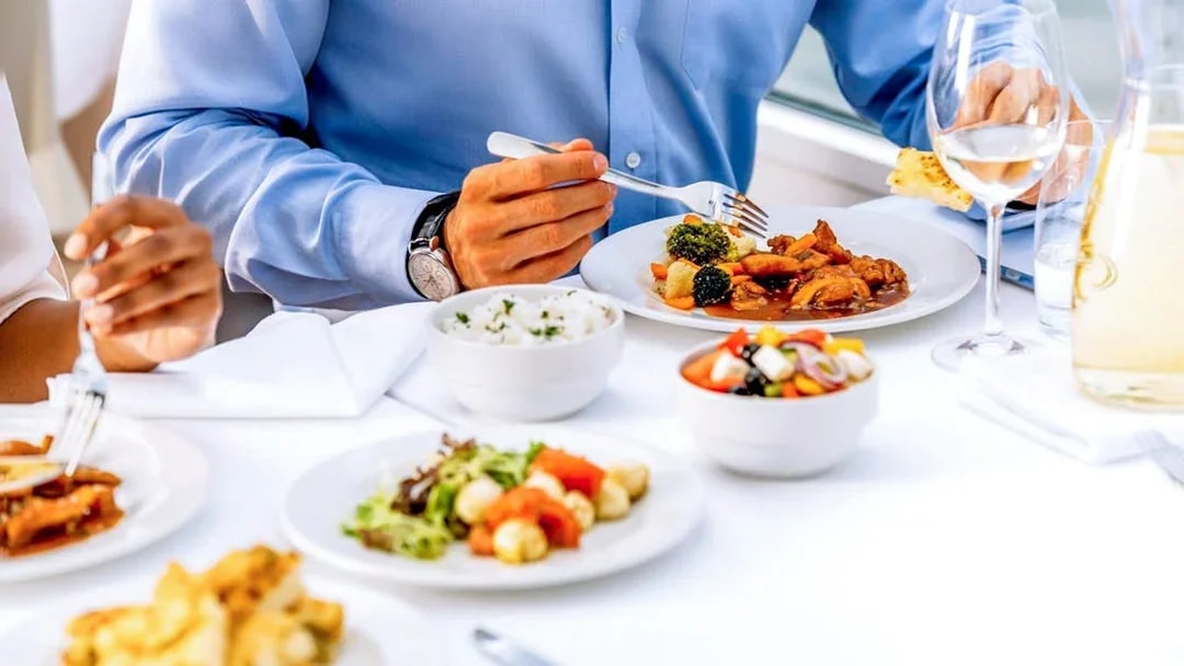 Dining experience on Vltava River cruise with plates of food and wine glasses.
