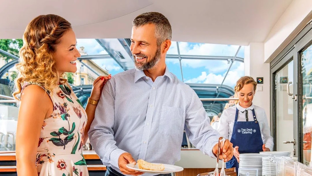 Couple enjoying buffet on Vltava River sightseeing cruise in Prague.