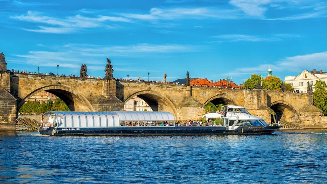 Vltava River cruise boat passing under Charles Bridge in Prague.