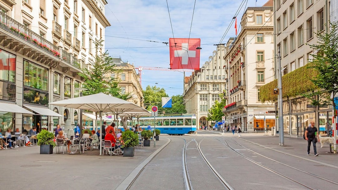 Zürich city street with tram, Swiss flag, and outdoor café.