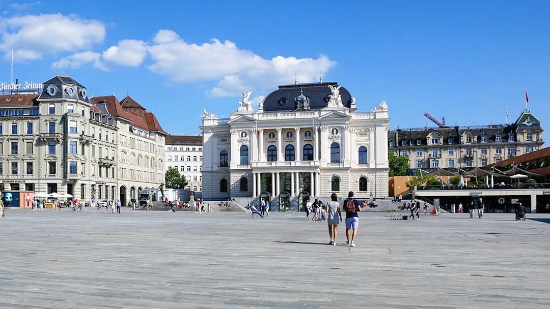 Zürich Opera House with people walking in Sechseläutenplatz on a sunny day.