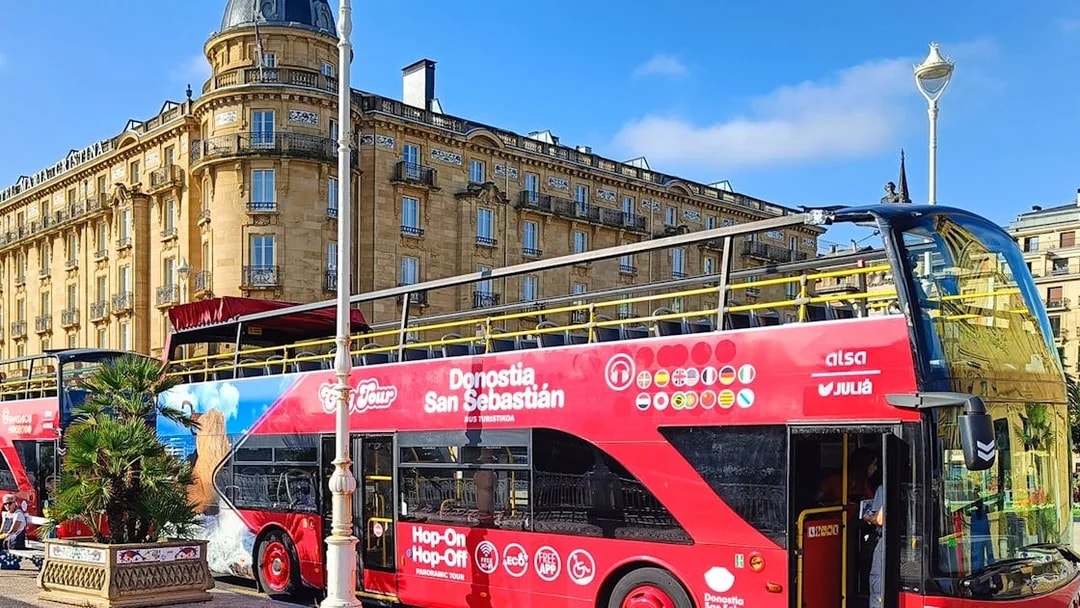 Hop-on hop-off tour bus in front of historic building in San Sebastian.
