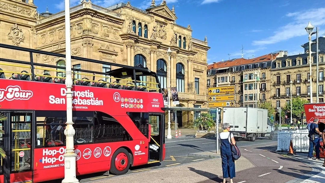 Hop-on hop-off tour bus in front of San Sebastian's historic building.