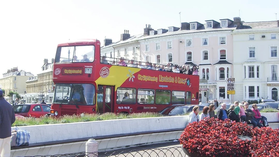 Open-top sightseeing bus in Llandudno, Wales, with tourists enjoying the view.
