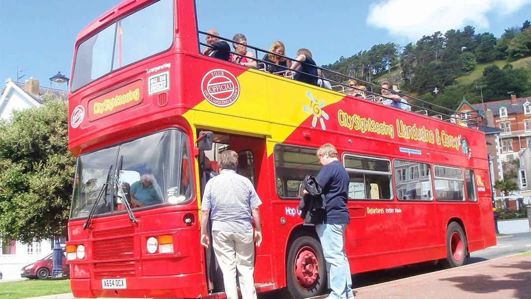Open-top sightseeing bus in Llandudno, passengers boarding for a 24-hour hop-on-hop-off tour.
