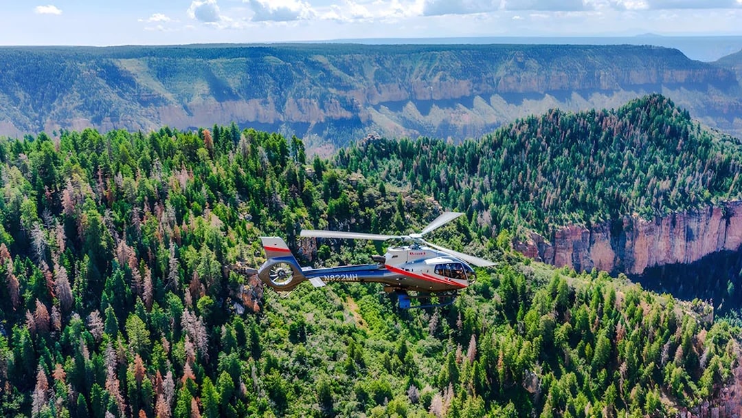 Helicopter flying over Grand Canyon National Park with forested cliffs below.
