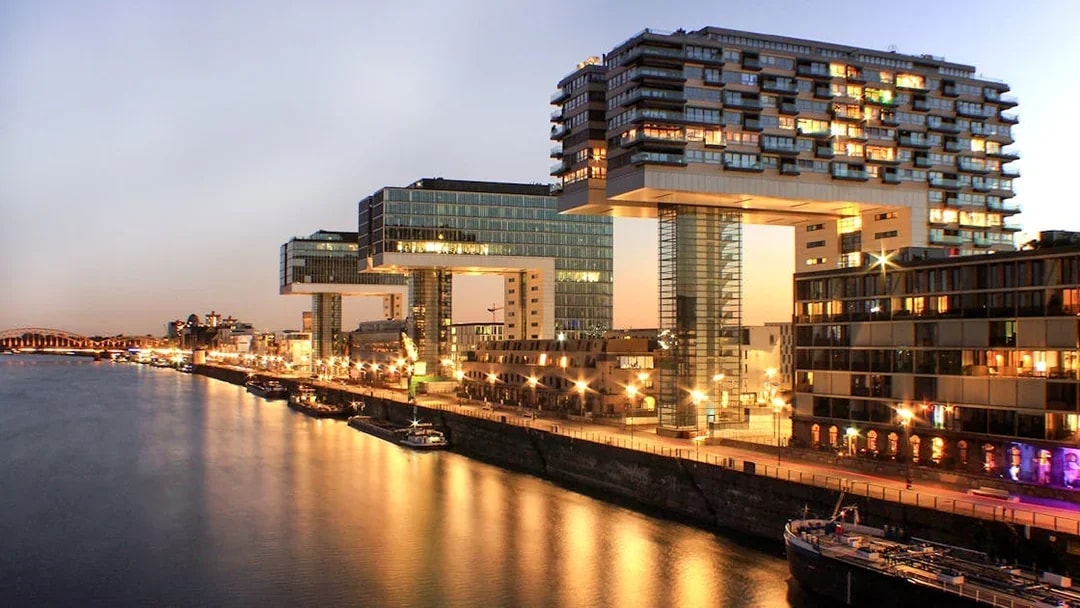 Evening view of Cologne's Rheinauhafen district with illuminated Kranhäuser buildings.