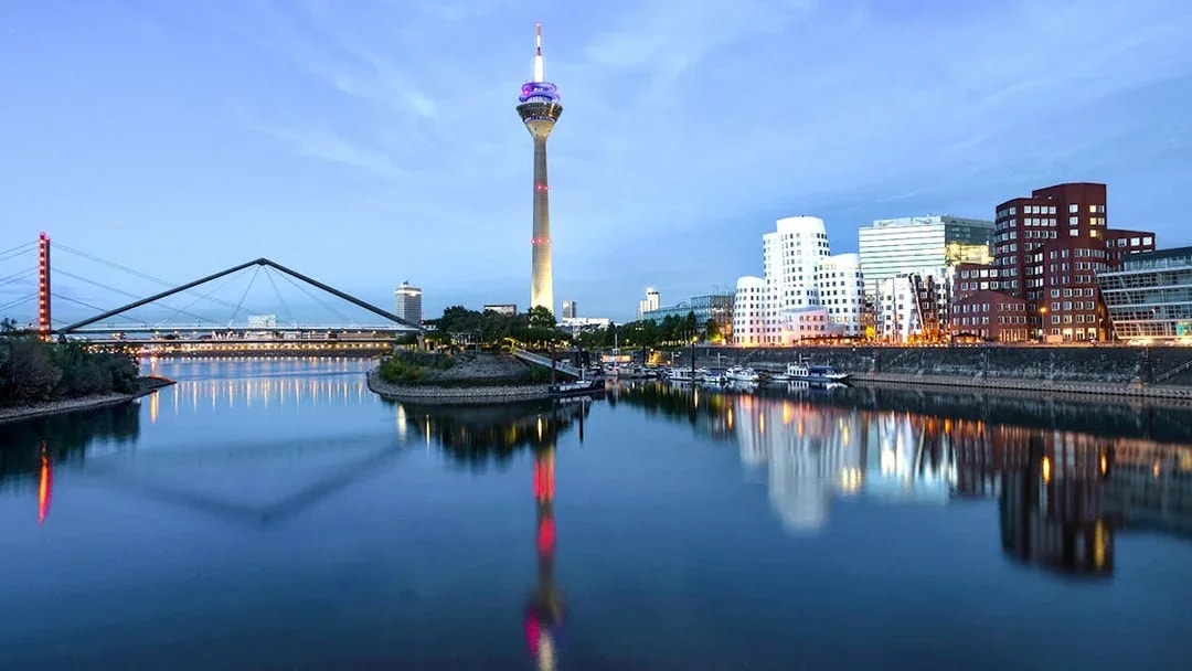 Evening view of Düsseldorf skyline with Rheinturm and bridge reflecting in the Rhine River.
