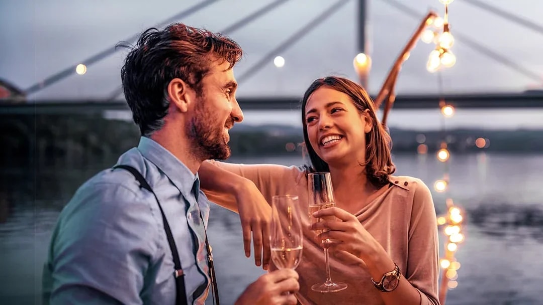 Couple enjoying champagne on an evening cruise in Düsseldorf with bridge lights in the background.