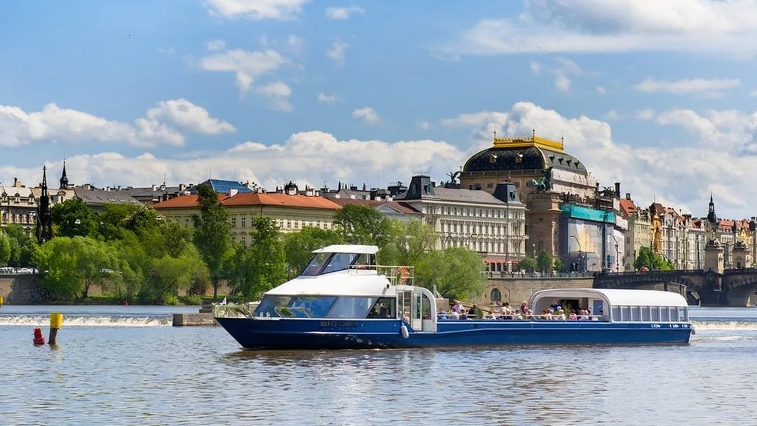 Sightseeing cruise on Vltava River with historic Prague buildings in the background.