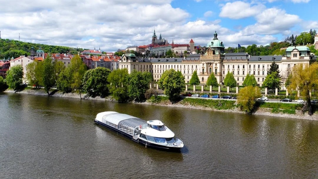 River cruise boat on Vltava River with Prague Castle in the background.