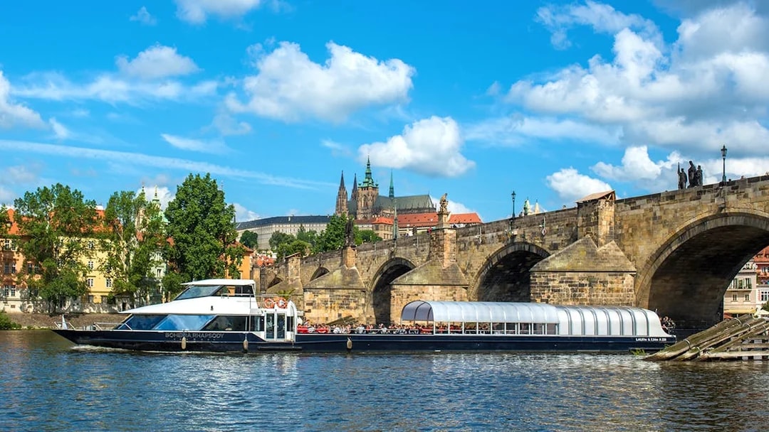 Vltava River cruise boat passing under Charles Bridge in Prague.