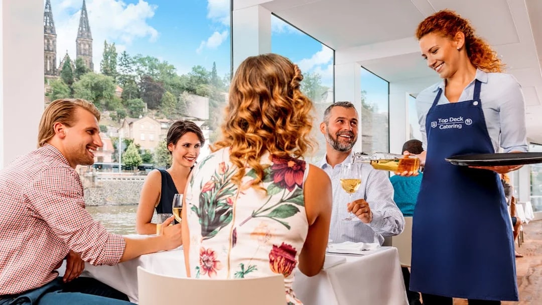 Guests enjoying lunch with wine on a Prague river cruise, with live music and city views.