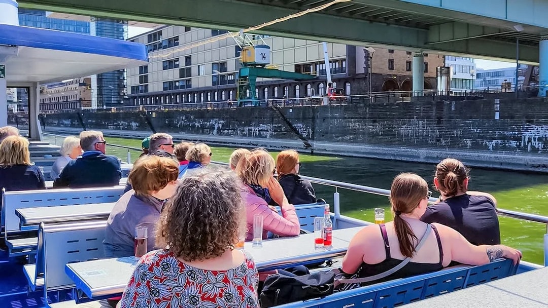 Cruise passengers on deck viewing Cologne harbor buildings.
