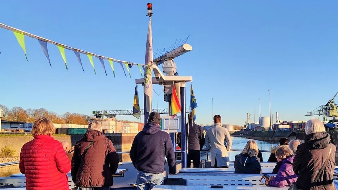 Tourists on a boat during a Cologne Harbour tour, with industrial cranes and containers in the background.