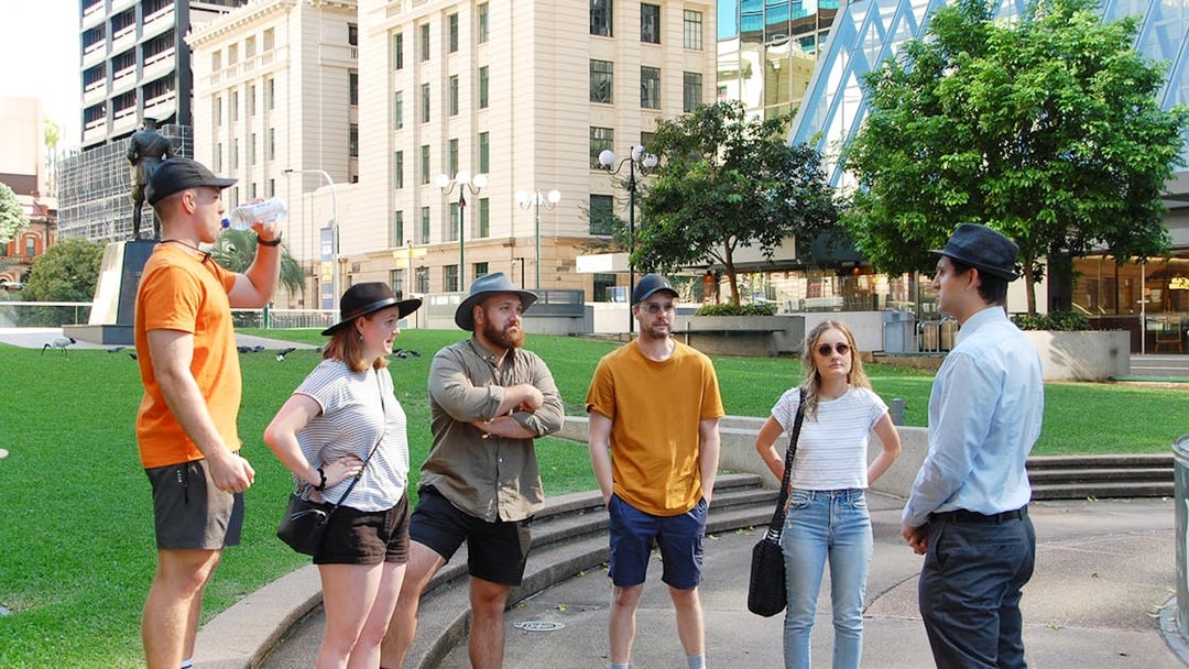Group of tourists listening to a guide in a Brisbane park during a walking tour.