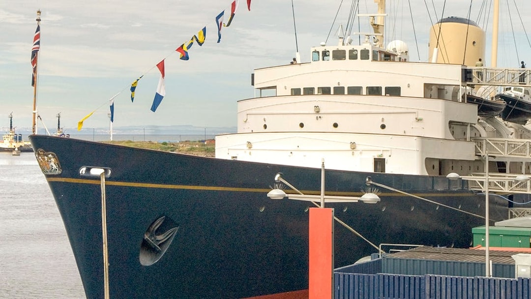 Royal Yacht Britannia docked with flags displayed.