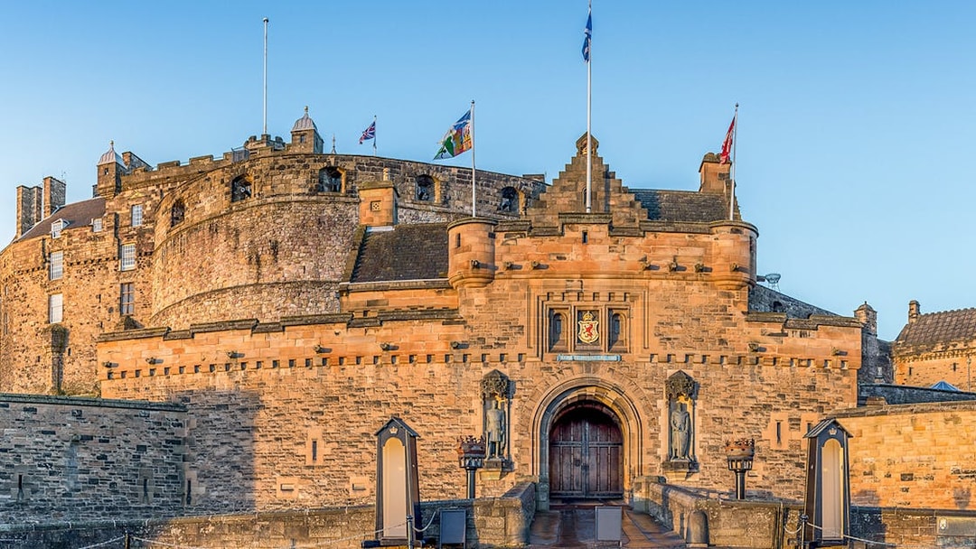 Edinburgh Castle front gate with stone walls and flags flying above.