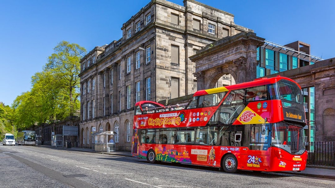 Edinburgh sightseeing bus in front of historic building on a sunny day.