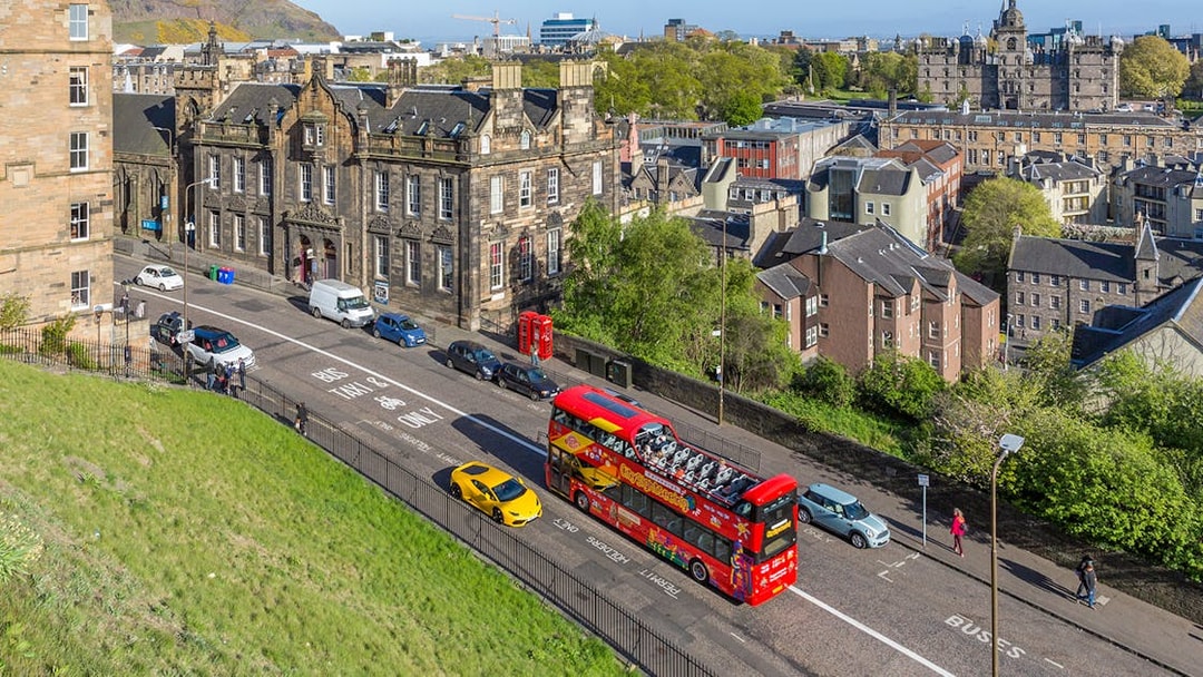 HOHO bus on street near Edinburgh Castle with cityscape in background.