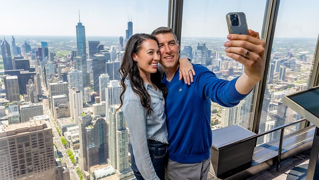 Couple taking a selfie at Chicago 360 Observation Deck with city skyline view.