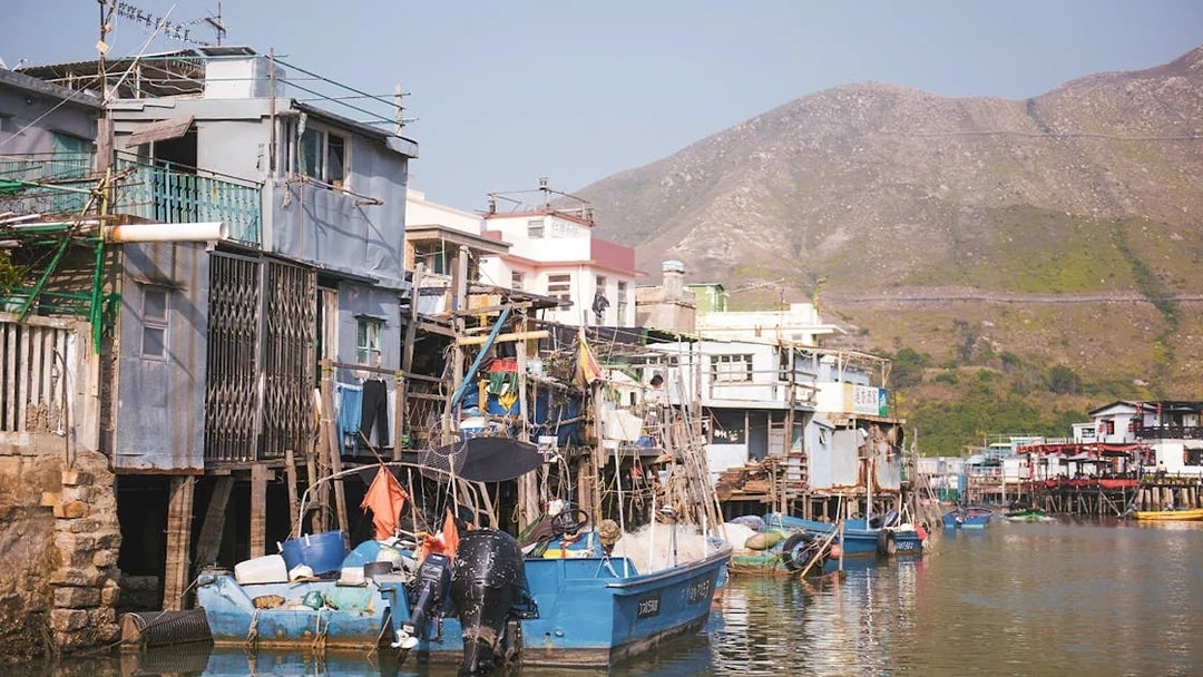 Stilt houses and fishing boats in Tai O village, Hong Kong, with mountains in the background.