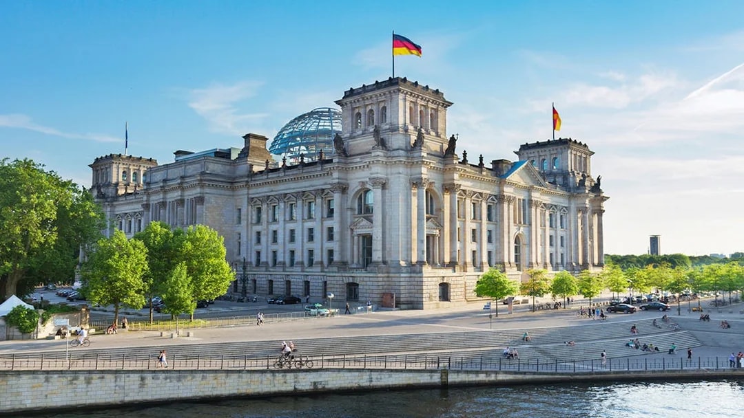 Reichstag building in Berlin's Government District with people and river in foreground.
