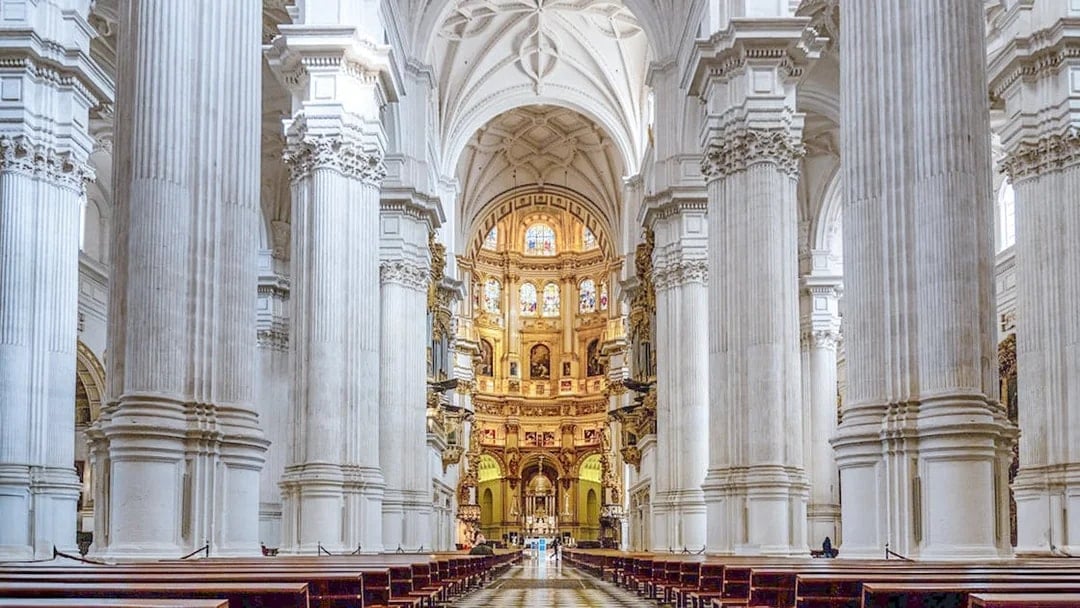 Granada Cathedral interior with ornate columns and stained glass windows.