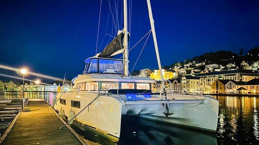 Luxury Catamaran Arctic Princess docked at night in a scenic harbor.