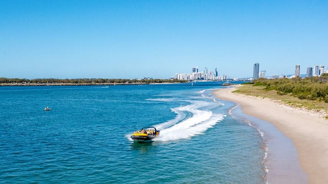 Jet boat speeding along Gold Coast shoreline with city skyline in background.