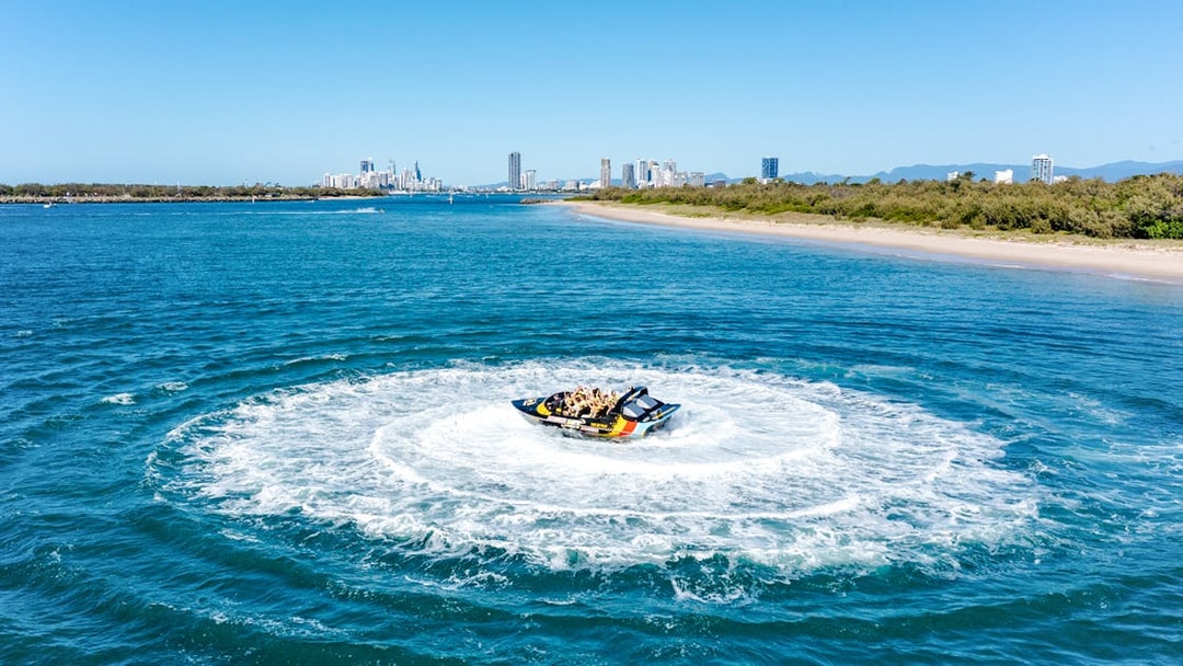 Jet boat making a circular splash on Gold Coast water with city skyline in background.