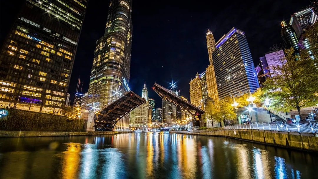 Chicago River at night with open lift bridge and illuminated skyline during architecture cruise.
