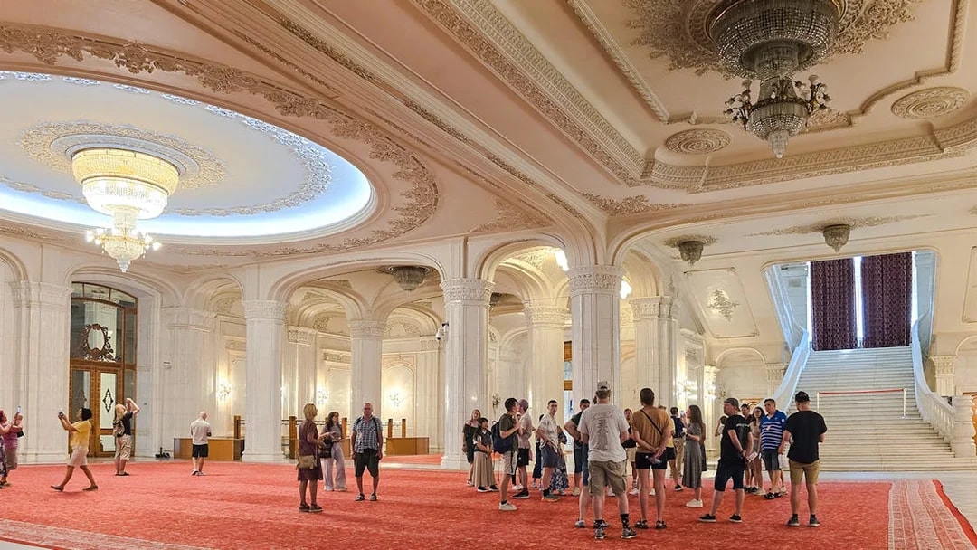 Guided tour group in the grand hall of the Palace of Parliament, near the staircase.