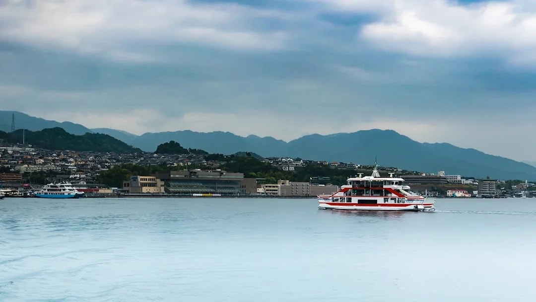 Ferry crossing Seto Inland Sea with Hiroshima cityscape and mountains in background.