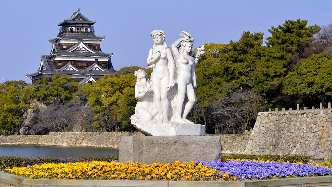 Hiroshima Castle with a statue and colorful flowers in the foreground, Japan.