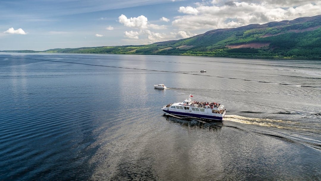 Cruise ship on Loch Ness, Scotland with scenic hills in the background.