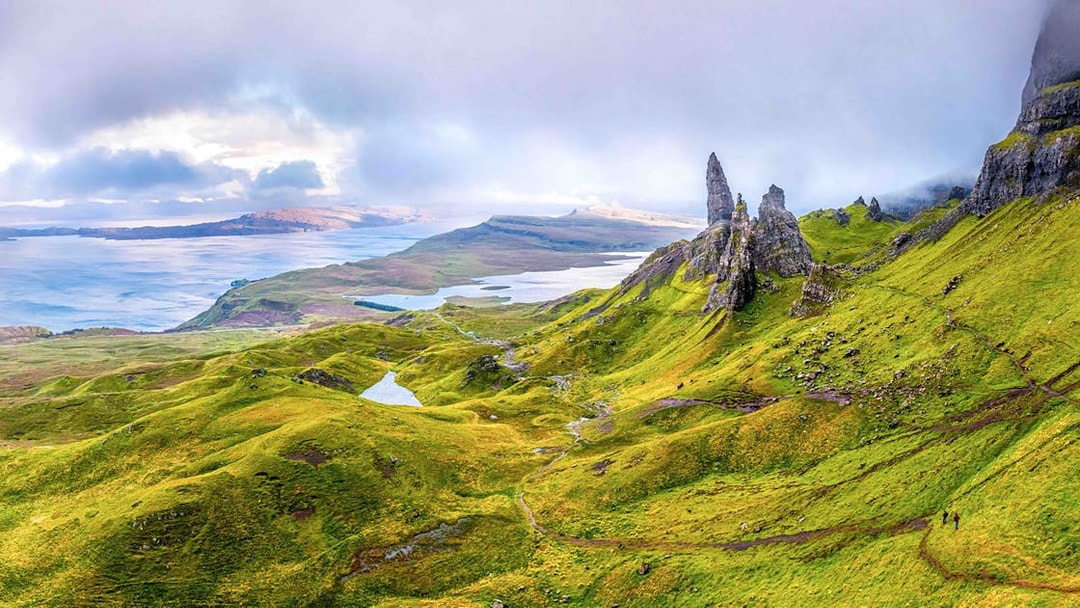 Loch Ness with lush green hills and rocky formations under a cloudy sky.