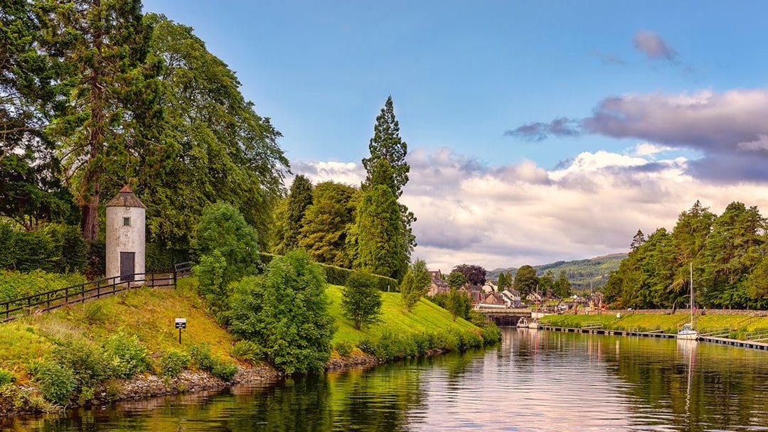 Caledonian Canal with lush greenery and a small tower near the water.