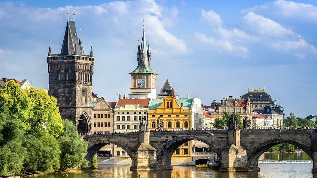 Charles Bridge over Vltava River in Prague with historic towers and buildings in the background.