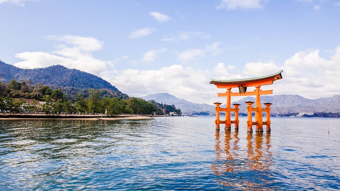 Torii gate at Itsukushima Shrine in Hiroshima, Japan, with mountains in the background.