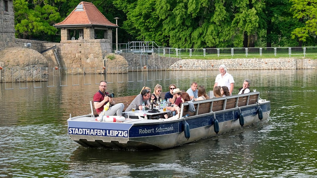 Guests on a motorboat tour of Karl Heine Canal in Leipzig, passing stone buildings and greenery.