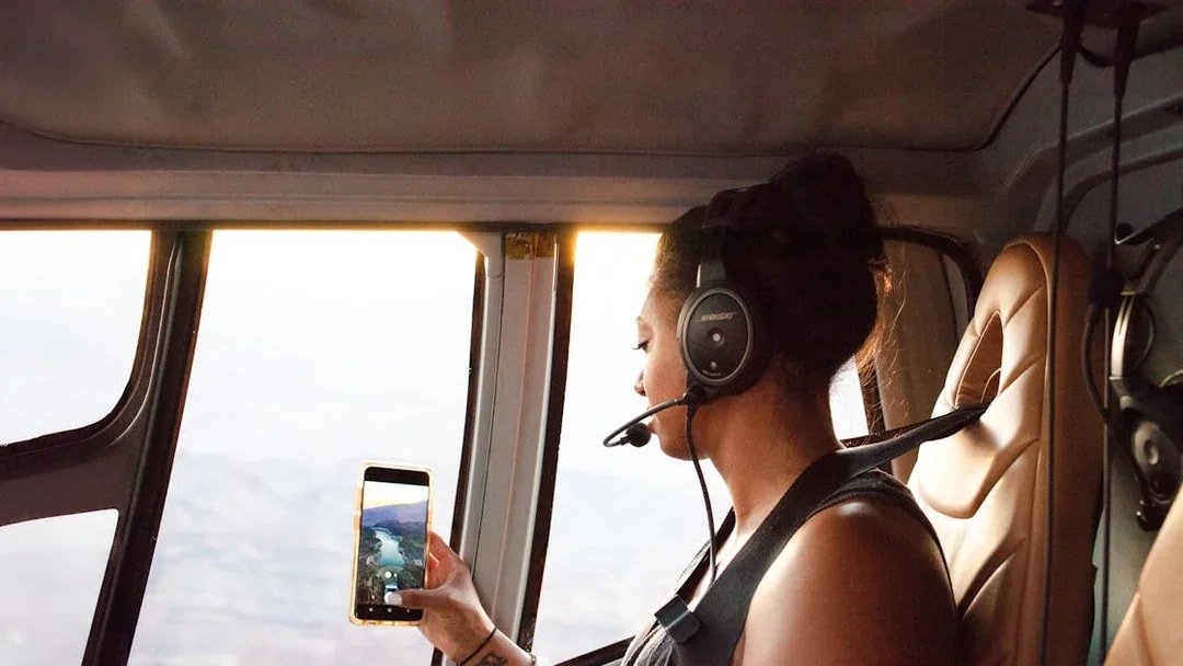 Woman taking a photo from inside a helicopter with a headset on.