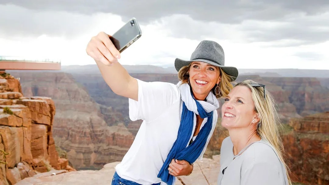 Two women taking a selfie at the Grand Canyon Skywalk with canyon view.
