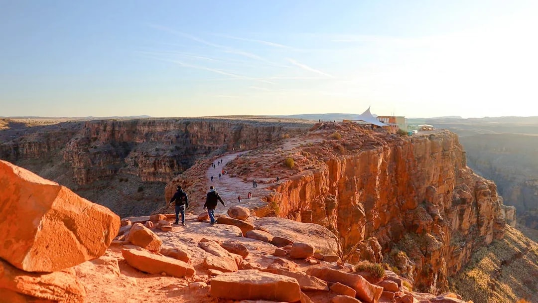 Grand Canyon West Rim with visitors walking along the cliff edge at sunset.