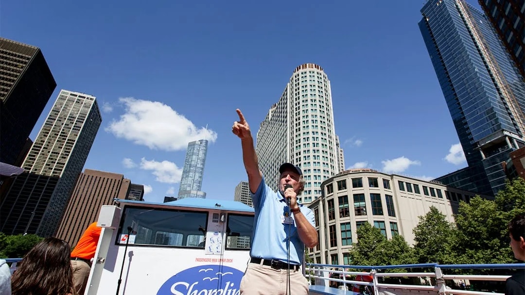 Tour guide speaking on a Chicago River Architecture Cruise with skyscrapers in the background.