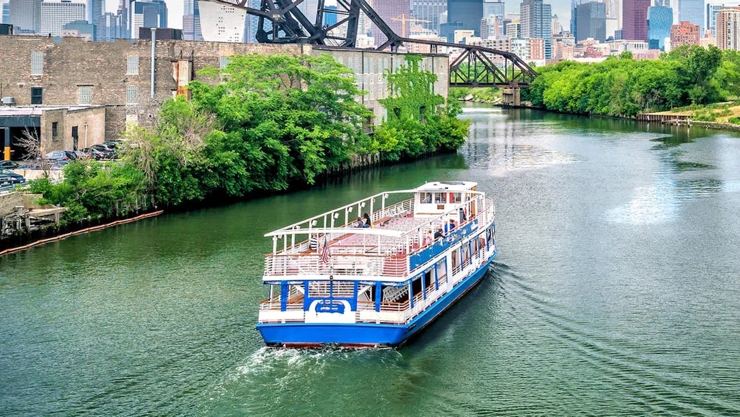 Tour boat cruising on the Chicago River with city skyline and bridge in the background.