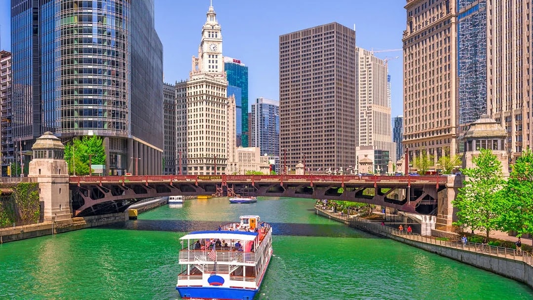 Cruise boat on Chicago River with city skyscrapers and Wrigley Building in view.