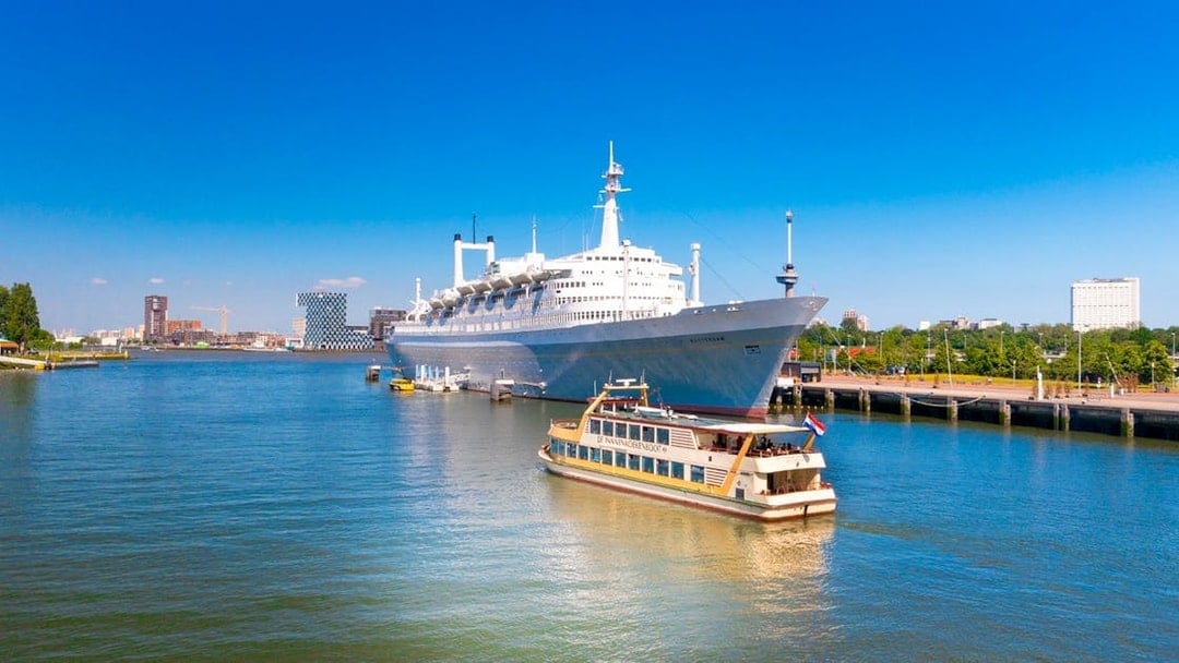 Pancake Cruise boat on Rotterdam harbor with a large ship in the background.
